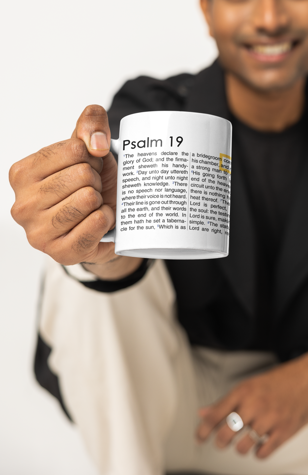 a man holding a coffee mug with a bible verse on it